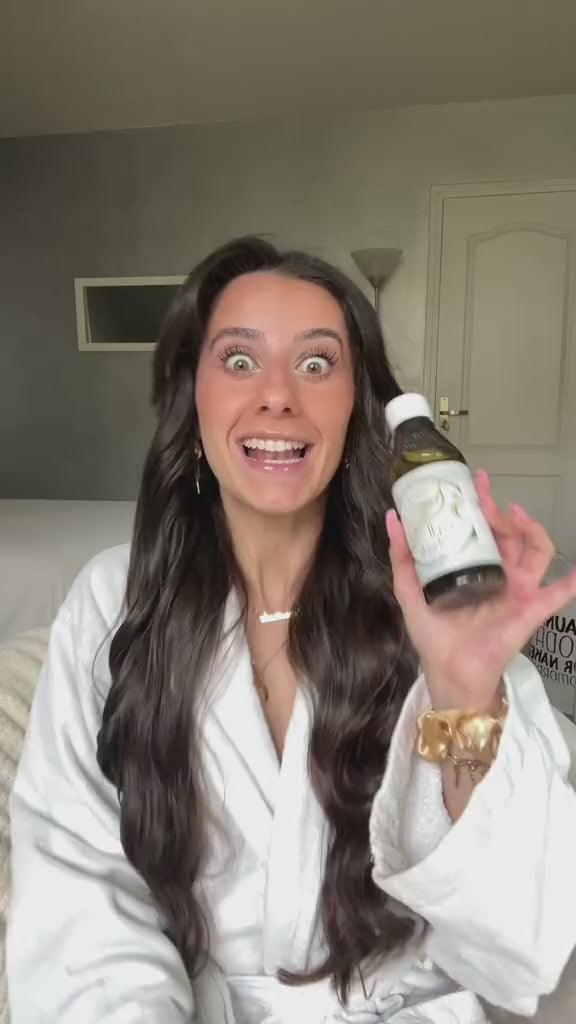 a brunette woman holds a bottle of afghani oil and describes its effects on her hair, 