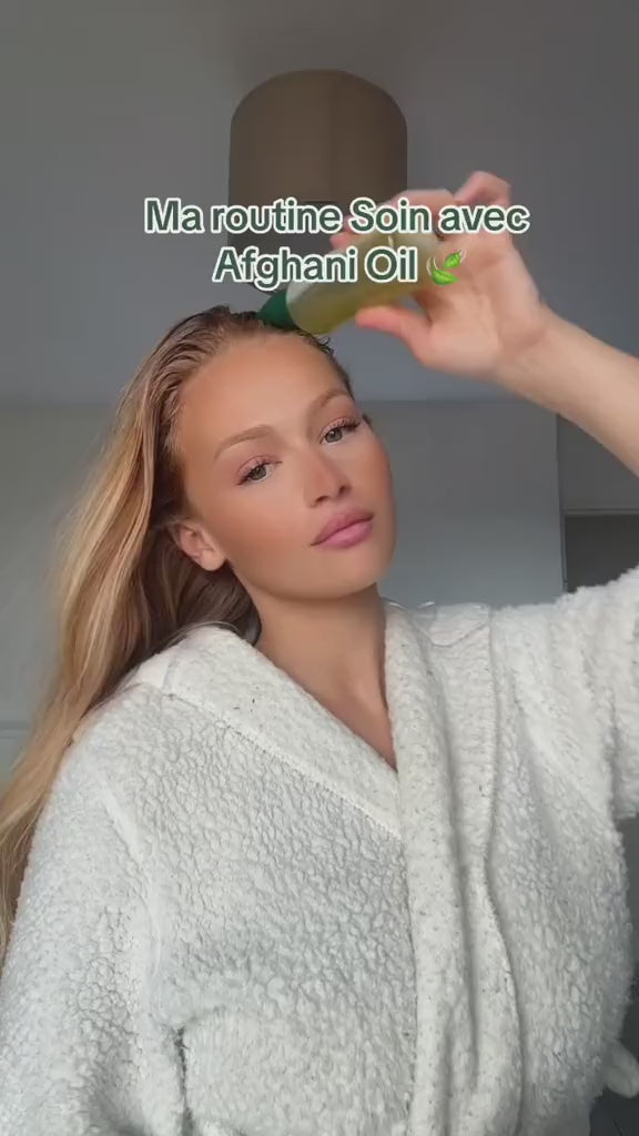 a woman in a white bathrobe pours afghani hair oil and describes it's effects on her hair , 